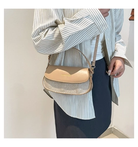 Detail einer beige Satteltasche mit Glitzer-Textur und goldenem Logo-Schriftzug