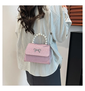 Detail of glitter pink shoulder bag with pearl handle and metal bow decoration
