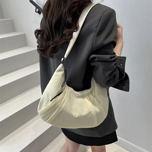 Grand sac fourre-tout croissant en nylon beige porté par un modèle dans un décor épuré