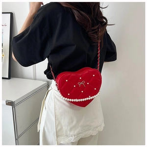 Detail of red heart-shaped quilted bag with bow, pearls and woven chain strap