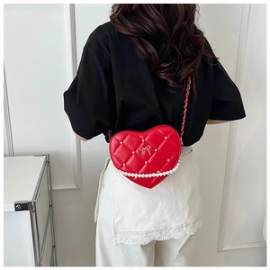 Rear view of heart-shaped red quilted crossbody bag with pearls and silver bow on model