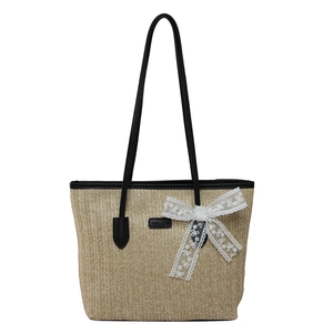 Large straw tote bag with black leather straps and a delicate white lace bow detail