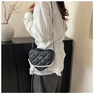 Detail view of heart-shaped quilted chain bag with pearl trim and bow accent on a model