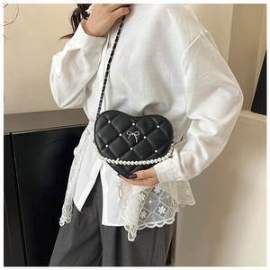 Detail of heart-shaped quilted bag with white pearls and a golden bow on the front