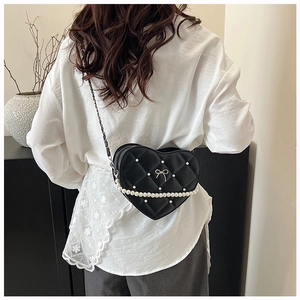 Detail of heart-shaped quilted bag with pearl accents and bow charm on a model