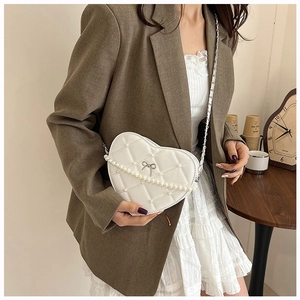 Close-up of white heart-shaped quilted bag with pearl metal chain and silver bow detail