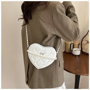 Detail of white heart quilted bag featuring pearl chain and silver bow on tan blazer
