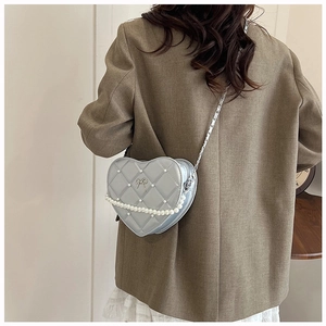 Detail of heart-shaped quilted bag with pearl chain strap worn over a brown blazer