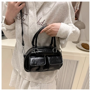 Detail of black patent leather Boston bag featuring decorative flap pockets and dual handles