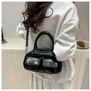 Crossbody view of a black patent leather tote bag with dual front pockets and silver hardware