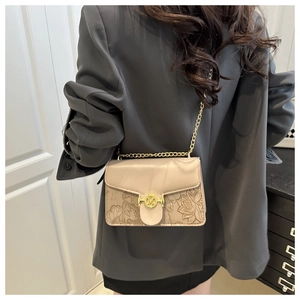 Detail showing the floral embossing and golden M-letter buckle on a beige chain bag