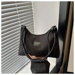 Detail of black pleated shoulder bag featuring textured vertical stripes and logo patch