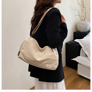 Détail du sac hobo en nylon beige avec logo métallique et étiquette mode sur fond épuré