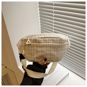 Close-up of beige plaid tweed saddle bag featuring white woven strap and black buckle