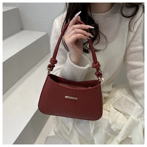 Détail du sac à main bordeaux à texture tissée avec poignée nouée et finitions dorées