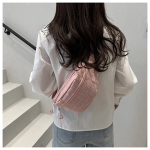 Detail of pink plaid waist bag with double zippers worn by model in a casual setting