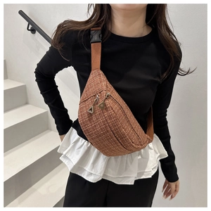 Detail of a brown woven tweed crossbody bag featuring metal zippers and nylon strap