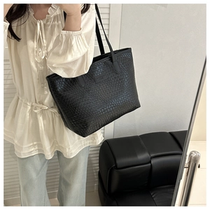 Close-up of black woven tote bag with slim shoulder straps and textured finish