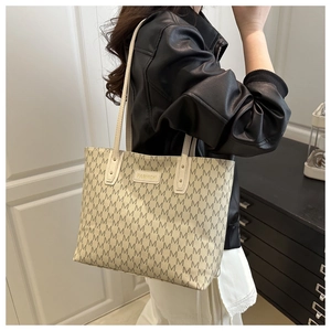 Détail du cabas beige avec imprimé M et plaque dorée porté sur une veste en cuir noir