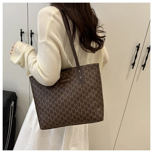 Sac fourre-tout marron à motif M avec plaque dorée porté à l'épaule par un mannequin