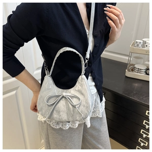 Sac à bandoulière argenté avec nœud porté par un mannequin, texture plissée et forme de lune