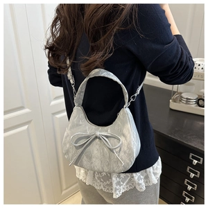 Gros plan d'un sac à main argenté en forme de croissant avec nœud et texture plissée