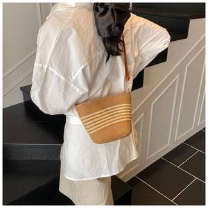 Détail du sac seau en paille tressée avec rayures blanches et bandoulière en cuir