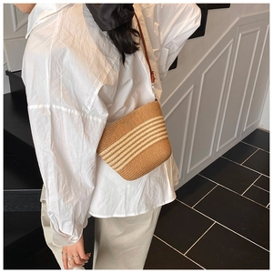 Detail of woven straw crossbody bag with white stripes and dark brown leather strap