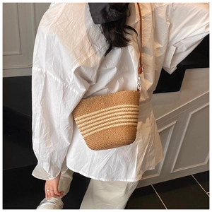 Detail of hand-woven straw bucket bag with white stripes and thin leather strap on model