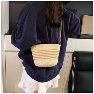 Detail of straw woven crossbody bag with brown stripes and a leather strap on a model
