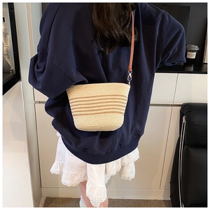 Detail of straw woven crossbody bag with brown stripes and leather strap on model
