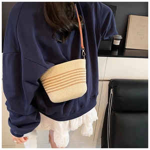Detail of woven straw bucket bag with earthy stripes and leather shoulder strap
