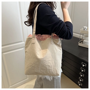 Detail of minimalist beige drawstring bucket bag with pink lining and pleated texture