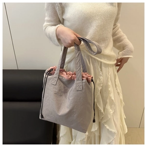 Detail of grey pleated drawstring bucket bag featuring a pink lining and nylon texture