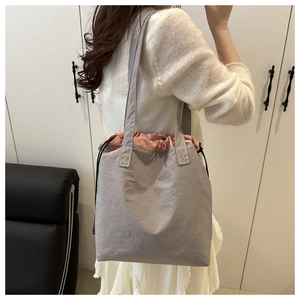 Detailed side view of large grey canvas tote bag with pink drawstring on a model