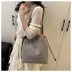 Detail of grey drawstring bucket bag with pink lining shown on model for size reference