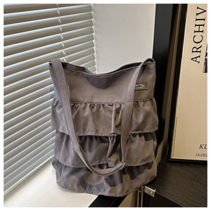 Detail of grey oxford tote bag featuring ruffled layers and a rectangular logo patch