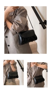 Detail of black pleated leather handbag featuring metal chain strap and modern texture