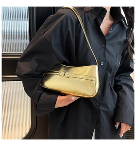 Metallic gold baguette shoulder bag with metal buckle shown in a stylish fashion context