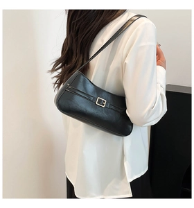 Side view of black faux leather baguette bag with metal buckle on a model shoulder
