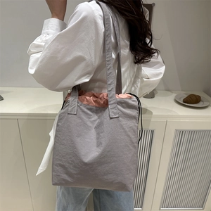 Gray nylon bucket bag with pink drawstring lining shown on a model in a minimalist setting