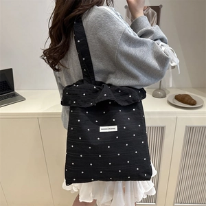 Black floral tote bag with ruffle trim and shoulder strap in a cozy lifestyle setting