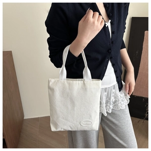 Detailed texture of off-white corduroy tote bag featuring a round logo patch and woven handles