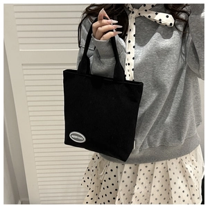 Detail of black corduroy striped handbag with white brand label and short handle strap