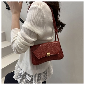 Detail of burgundy woven texture shoulder bag with gold clasp and knotted strap on model