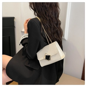 Detail showing the white crocodile textured bag with gold chain worn by a model