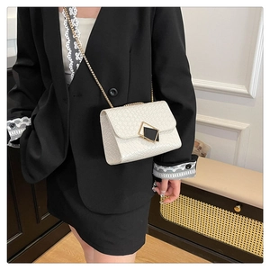 Close-up of white woven crossbody bag with gold chain strap and geometric metal buckle