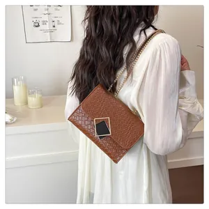 Detailed view of brown woven leather crossbody bag with gold chain strap on a model