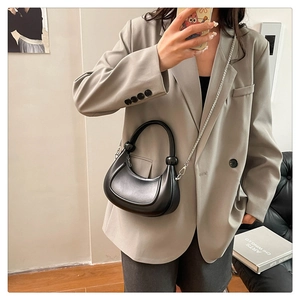 Detail of a black leather saddle bag featuring a unique bead handle and silver chain strap
