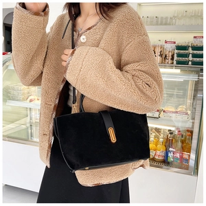 Detail of matte black tote bag with gold oval buckle shown on model in street scene